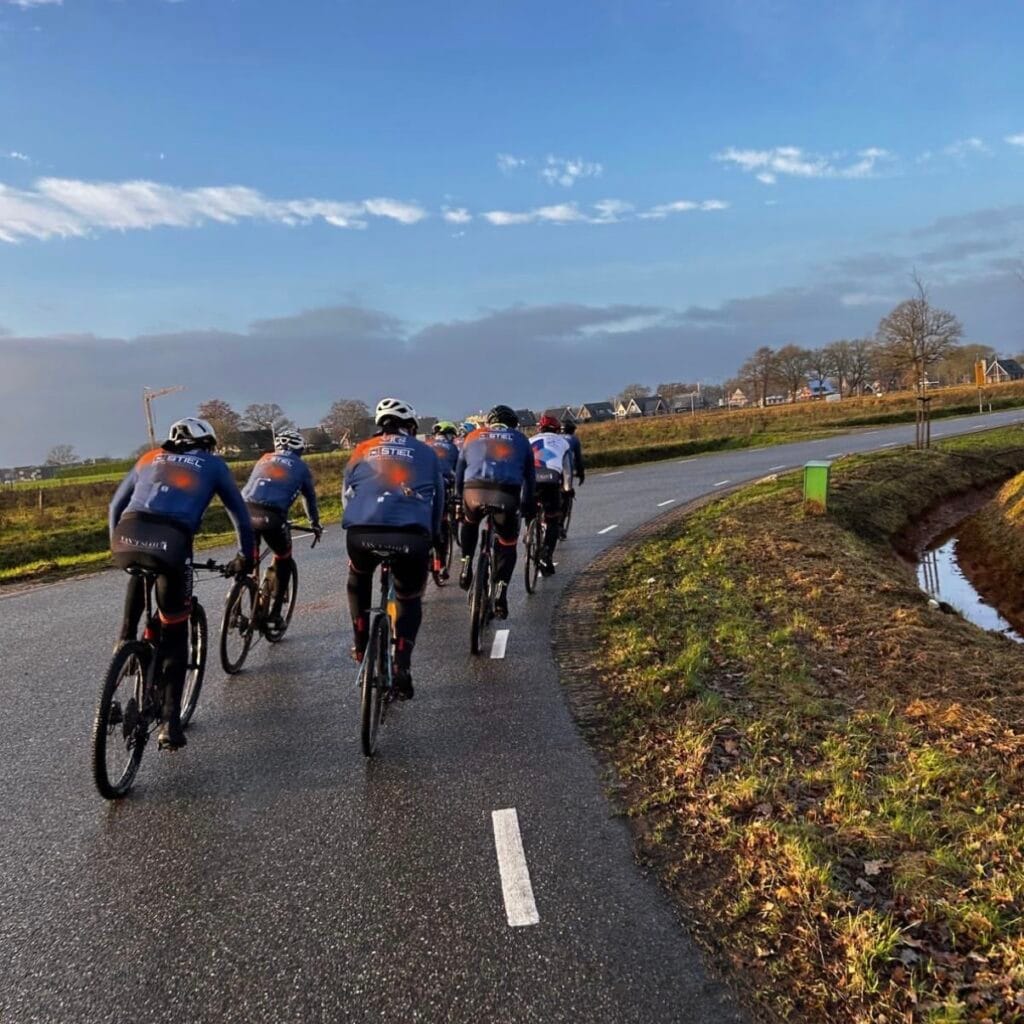 Groep wielrenners rijdt in de winterzon over een polderweg langs een sloot